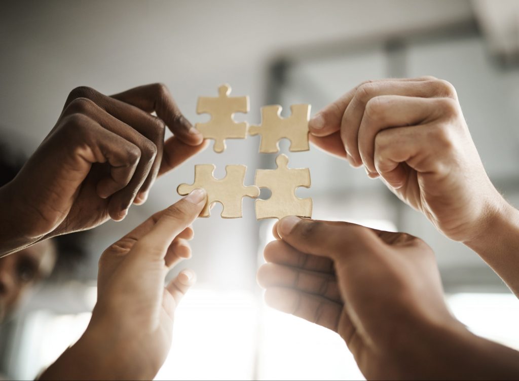 Cropped shot of a group of businesspeople completing a puzzle together in a modern office