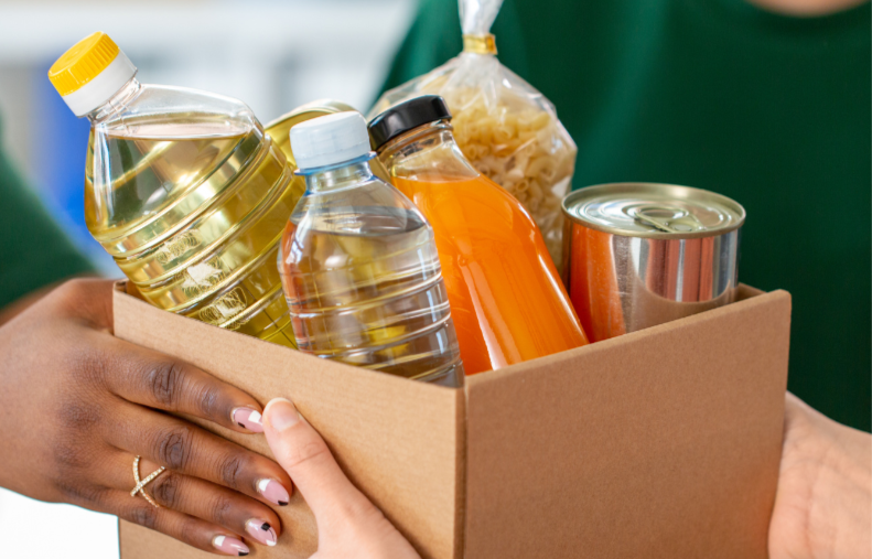 A volunteer handing off a box of food donations to a client. 
