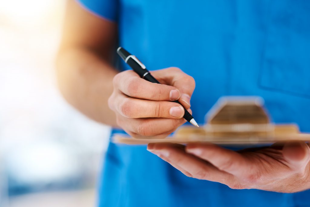 Cropped shot of a male nurse writing something on a clipboard.