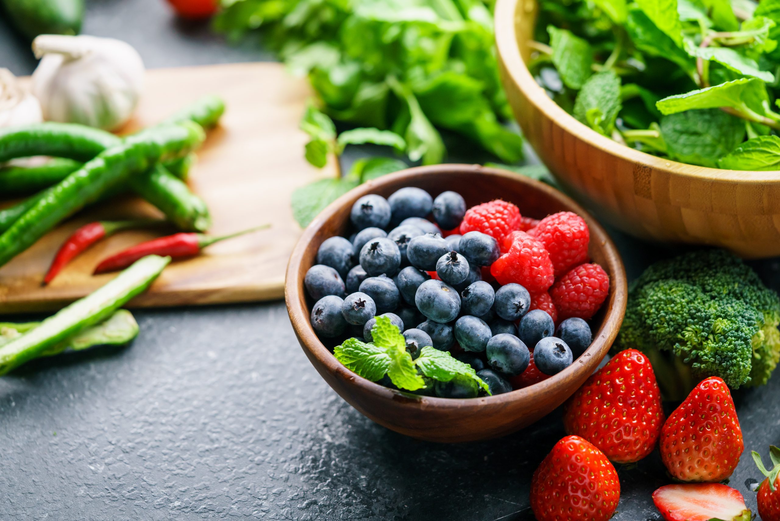 Image shows berries in a bowl and fresh vegetables beside it.