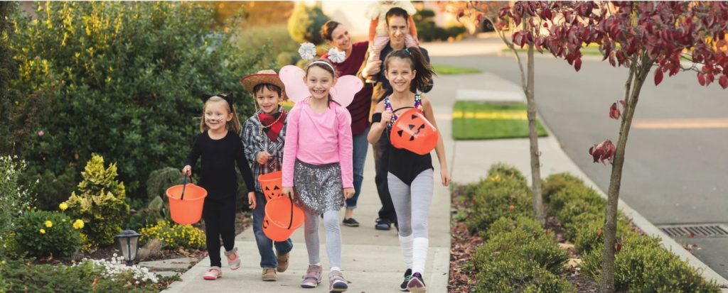 A group of children dressed in Halloween costumes walking on the sidewalk.