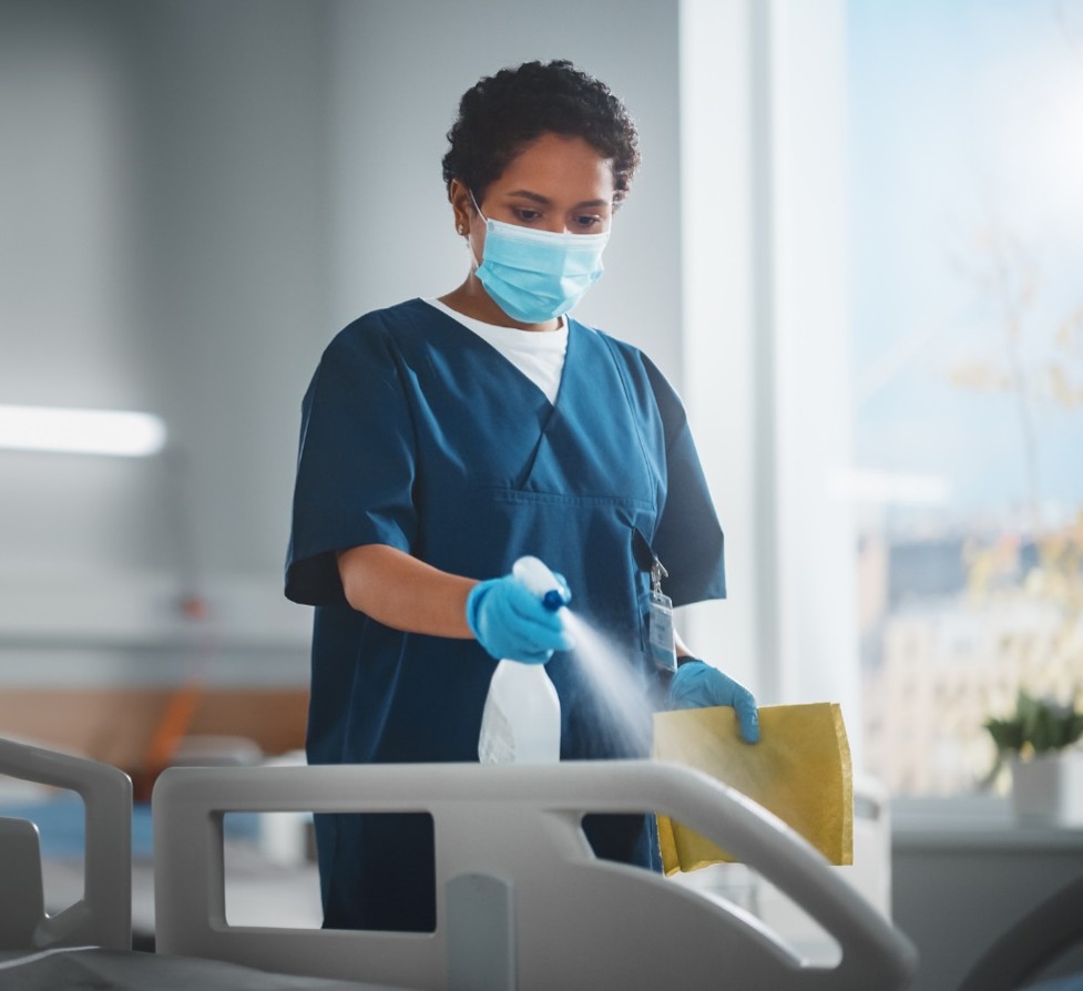 Hospital worker is disinfecting the rails to a hospital bed.
